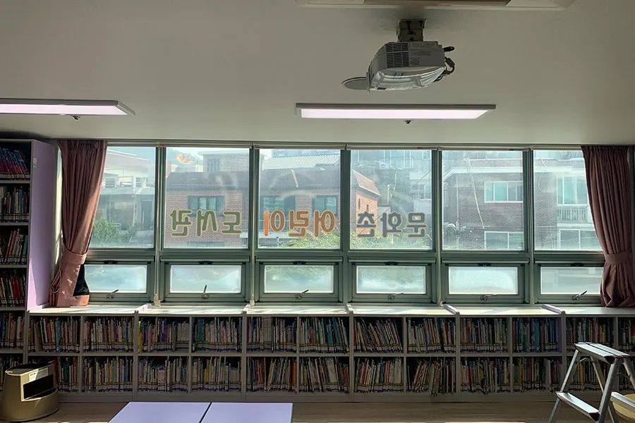 이어진 창문 구간을 순서대로 마감하는 시공 모습, 창밖으로 나무가 보이는 전경
