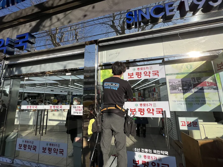 약국 내부에서 바라본 통유리 출입문, 손님들이 오가는 모습