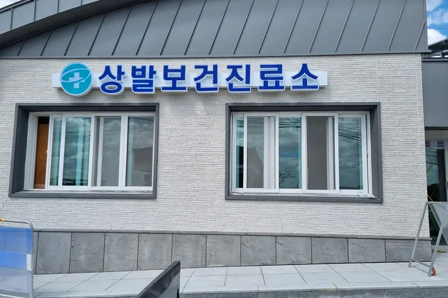 논밭을 배경으로 한 단층 건물 외관, 큰 창 두 개가 나란히 난 모습